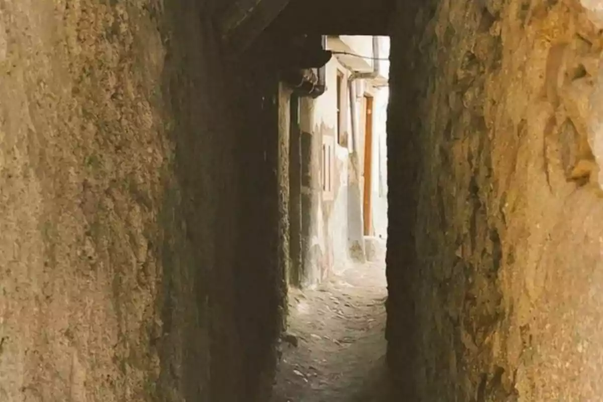 Un estrecho pasillo de piedra con paredes rústicas que conduce a una calle iluminada.