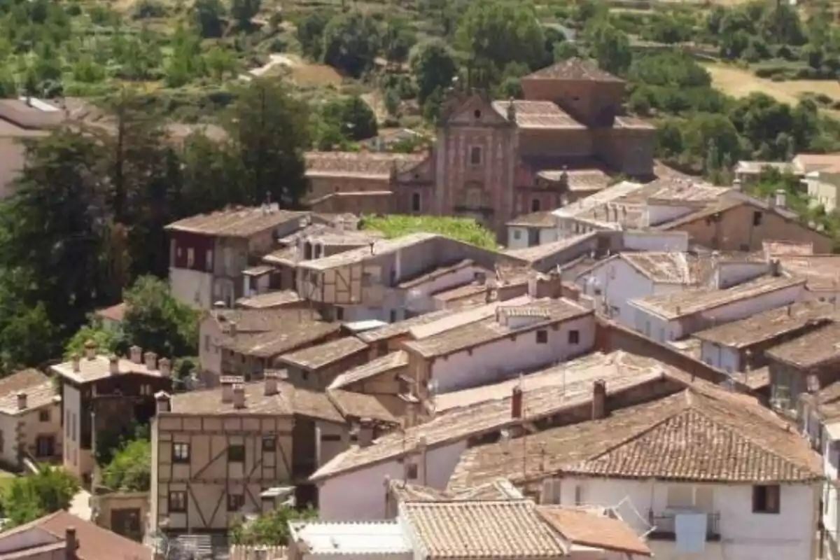 Vista panorámica de un pueblo con casas de tejados de tejas y una iglesia al fondo, rodeado de vegetación y colinas.