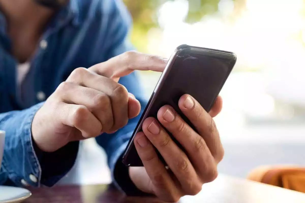 Manos de un hombre con camisa tejana usando un teléfono táctil Manos de un hombre con camisa tejana usando un teléfono táctil