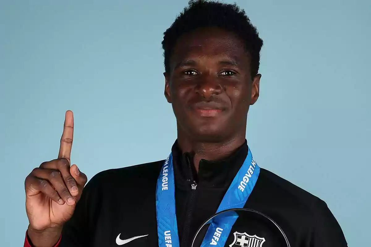 Young player with a blue medal and trophy raising an index finger pointing upward against a light blue background