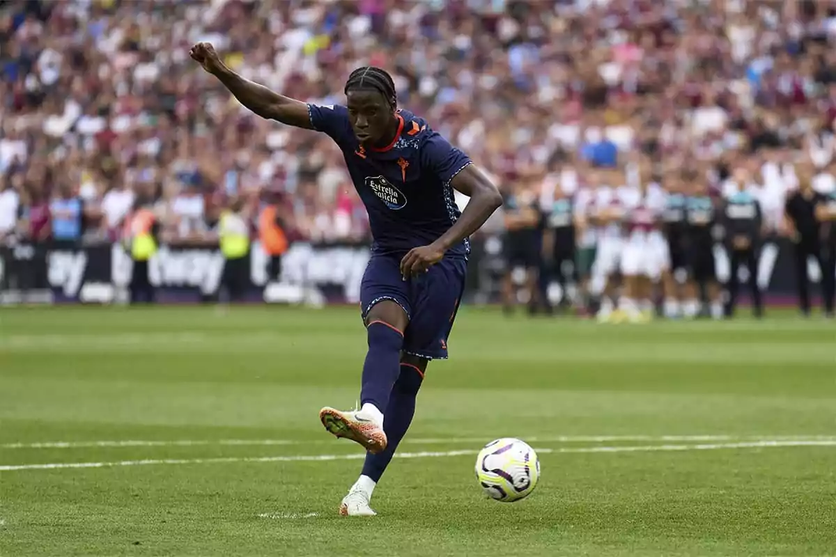 Soccer player in action during a match, wearing a dark blue uniform and kicking a ball on the field.