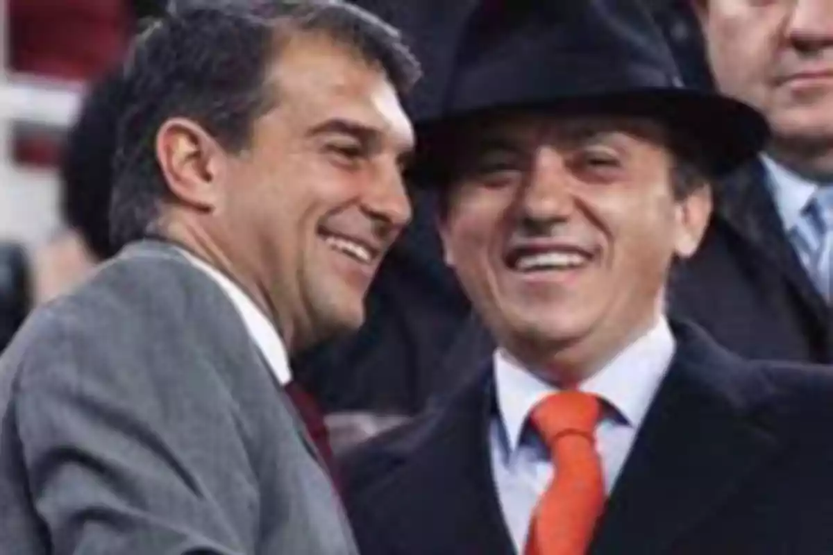 Two smiling men dressed in suits, one with a hat and orange tie.