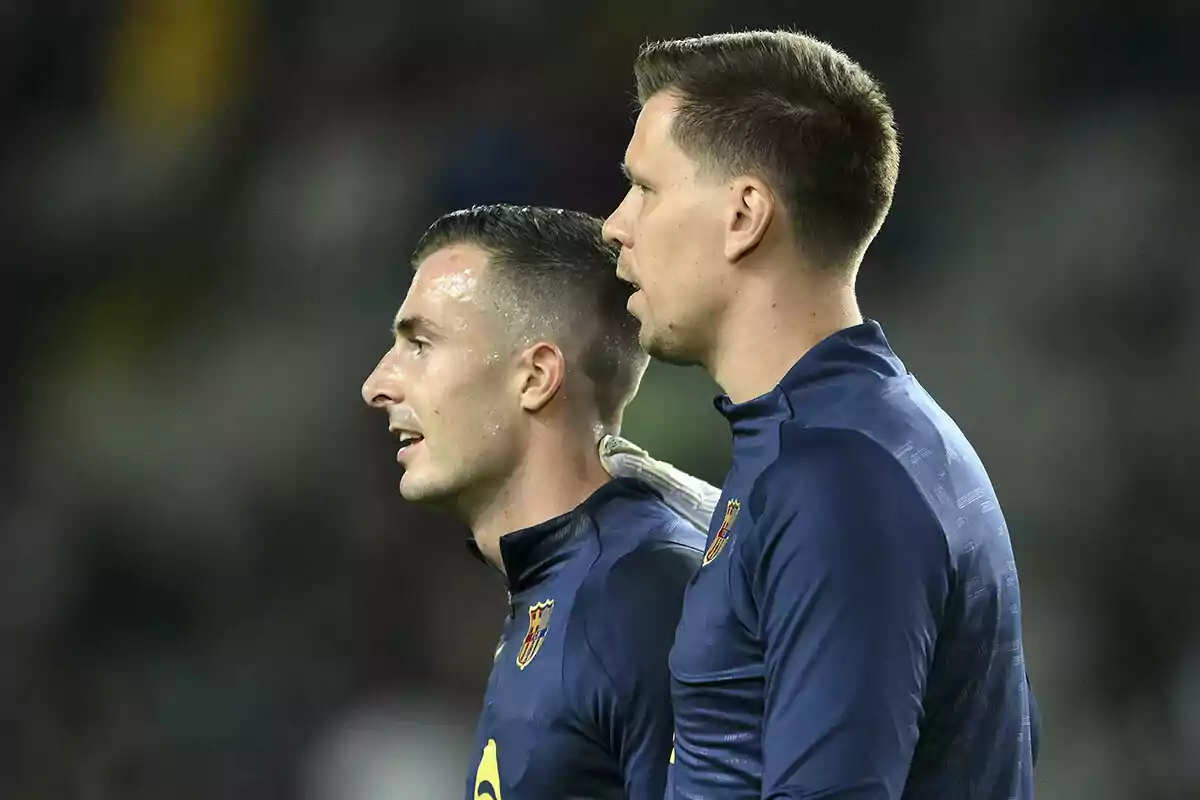 Dos jugadores de fútbol con uniformes oscuros observan atentamente algo fuera de la imagen. Dos jugadores de fútbol con uniformes oscuros observan atentamente algo fuera de la imagen.