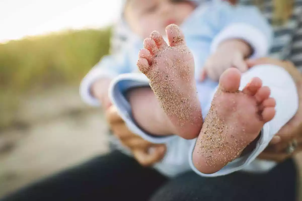 Imagen en la que se pueden ver los pies de un infante que está siendo sostenido por otra persona desde atrás Imagen en la que se pueden ver los pies de un infante que está siendo sostenido por otra persona desde atrás