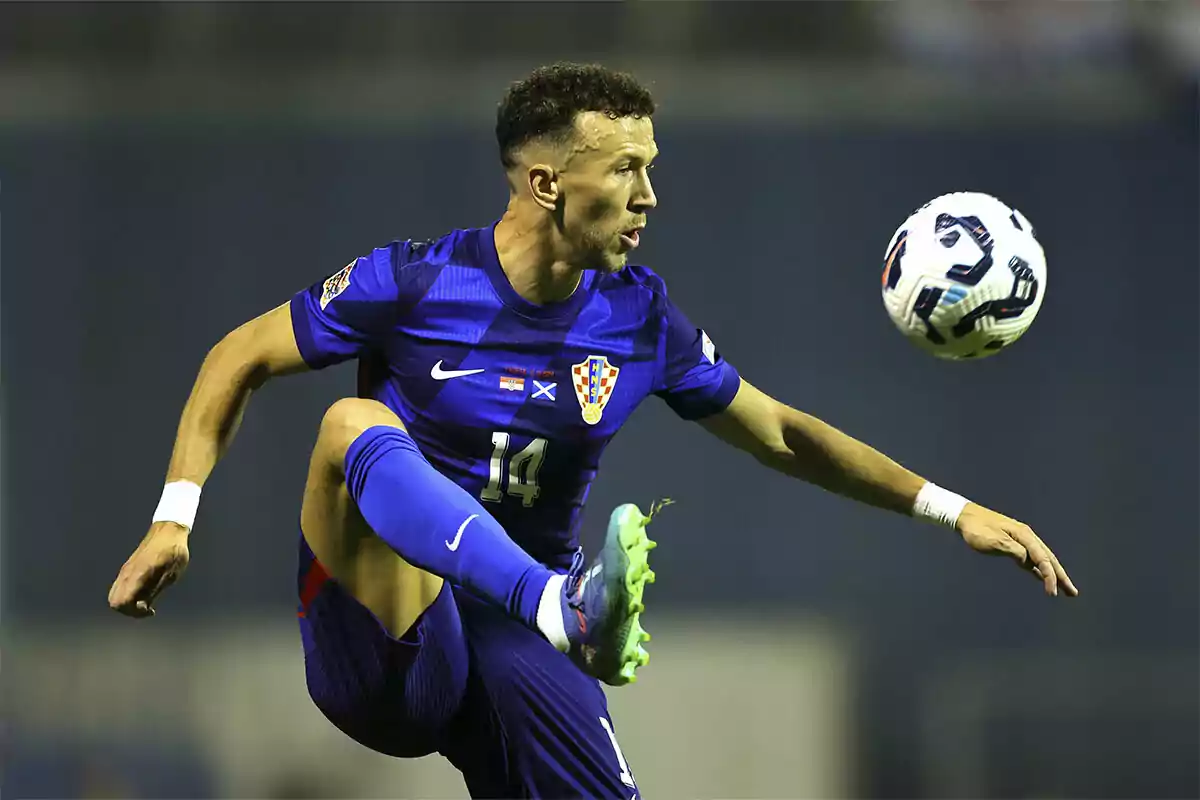 Futbolista croata con uniforme azul controlando el balón en el aire durante un partido Futbolista croata con uniforme azul controlando el balón en el aire durante un partido