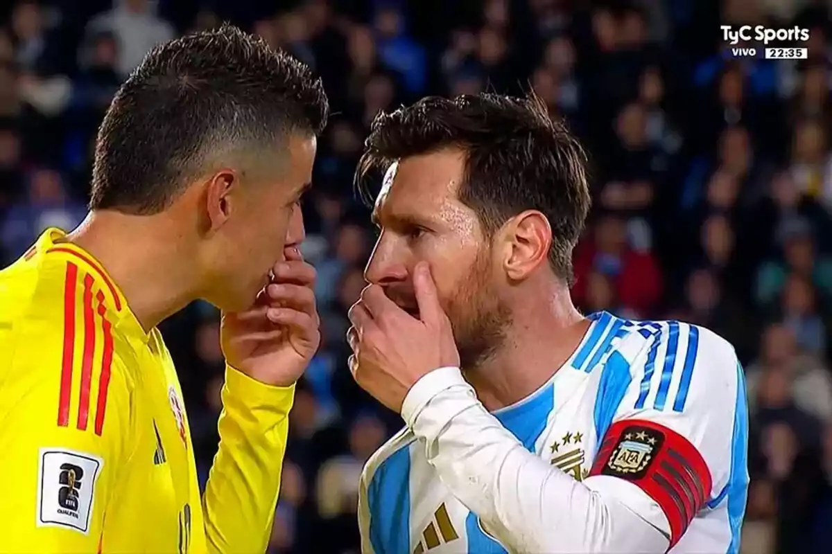 Dos futbolistas de las selecciones de Colombia y Argentina conversan en el campo cubriéndose la boca con la mano durante un partido