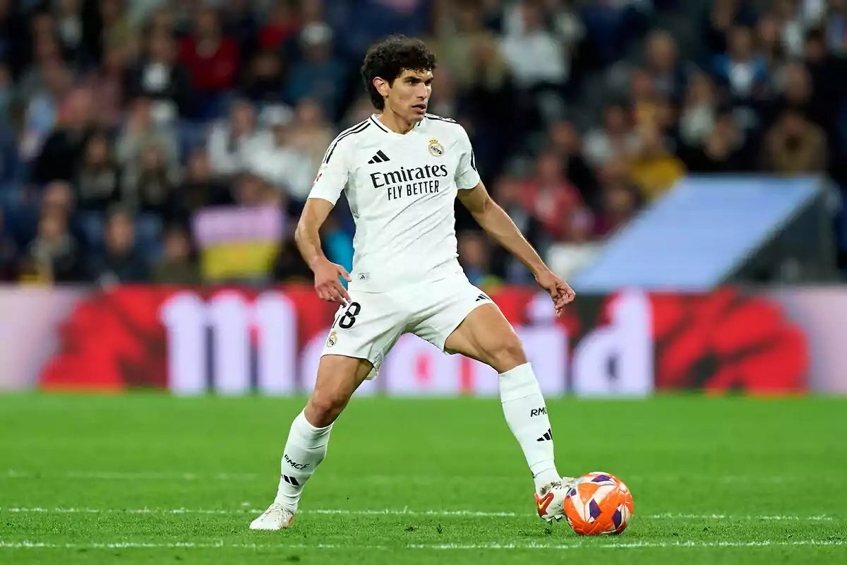 Un jugador de fútbol del Real Madrid en acción durante un partido, vistiendo el uniforme blanco del equipo y controlando el balón en el campo. Un jugador de fútbol del Real Madrid en acción durante un partido, vistiendo el uniforme blanco del equipo y controlando el balón en el campo.