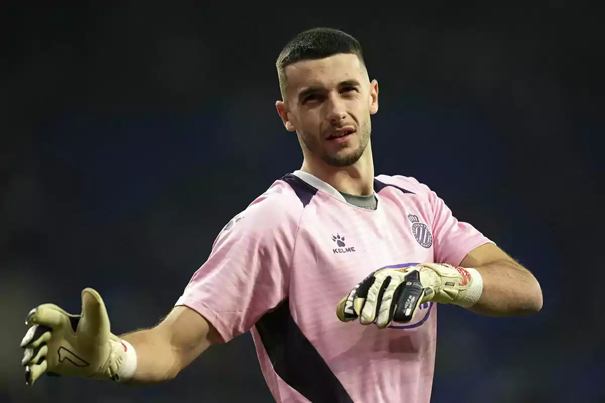 Un jugador de fútbol con uniforme rosa y guantes de portero en el campo.