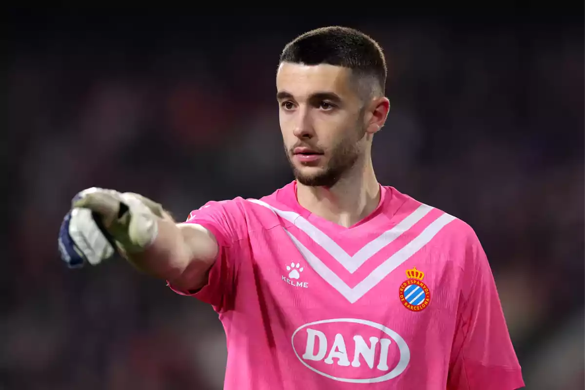 Soccer goalkeeper wearing a pink uniform and gloves pointing forward during a match