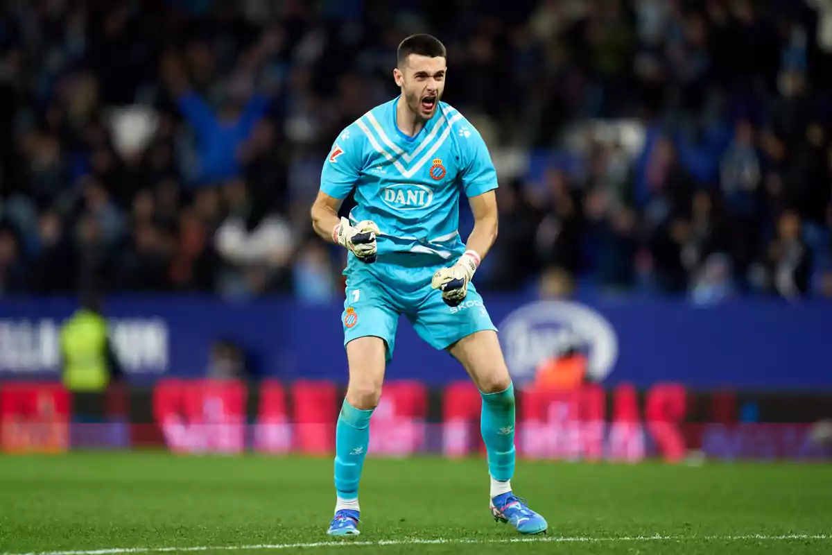 A player in a light blue uniform celebrates on the field during a match, with the blurred crowd in the background.