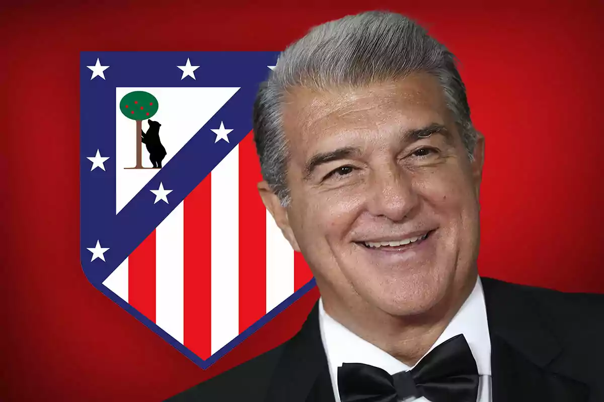 Un hombre sonriente con cabello canoso y traje formal frente al escudo del Atlético de Madrid sobre un fondo rojo.