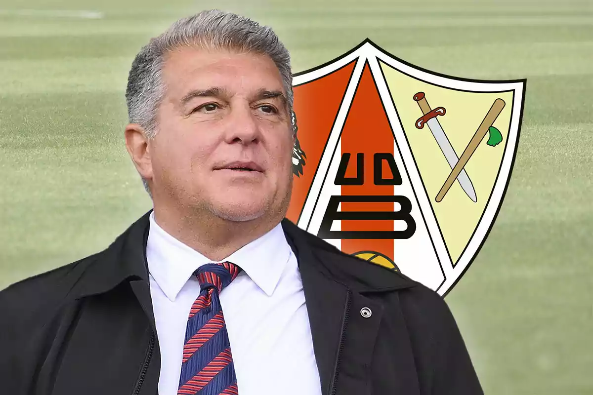 Joan Laporta con traje y corbata está de pie frente al escudo del UD Barbastro sobre un campo de césped.