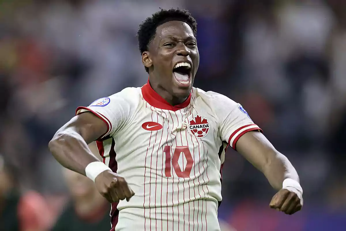 Soccer player celebrating enthusiastically during a match wearing a Canada jersey.