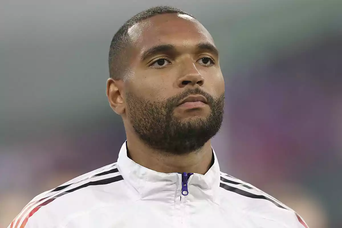 Jonathan Tah con chaqueta deportiva blanca y expresión seria. Jonathan Tah con chaqueta deportiva blanca y expresión seria.