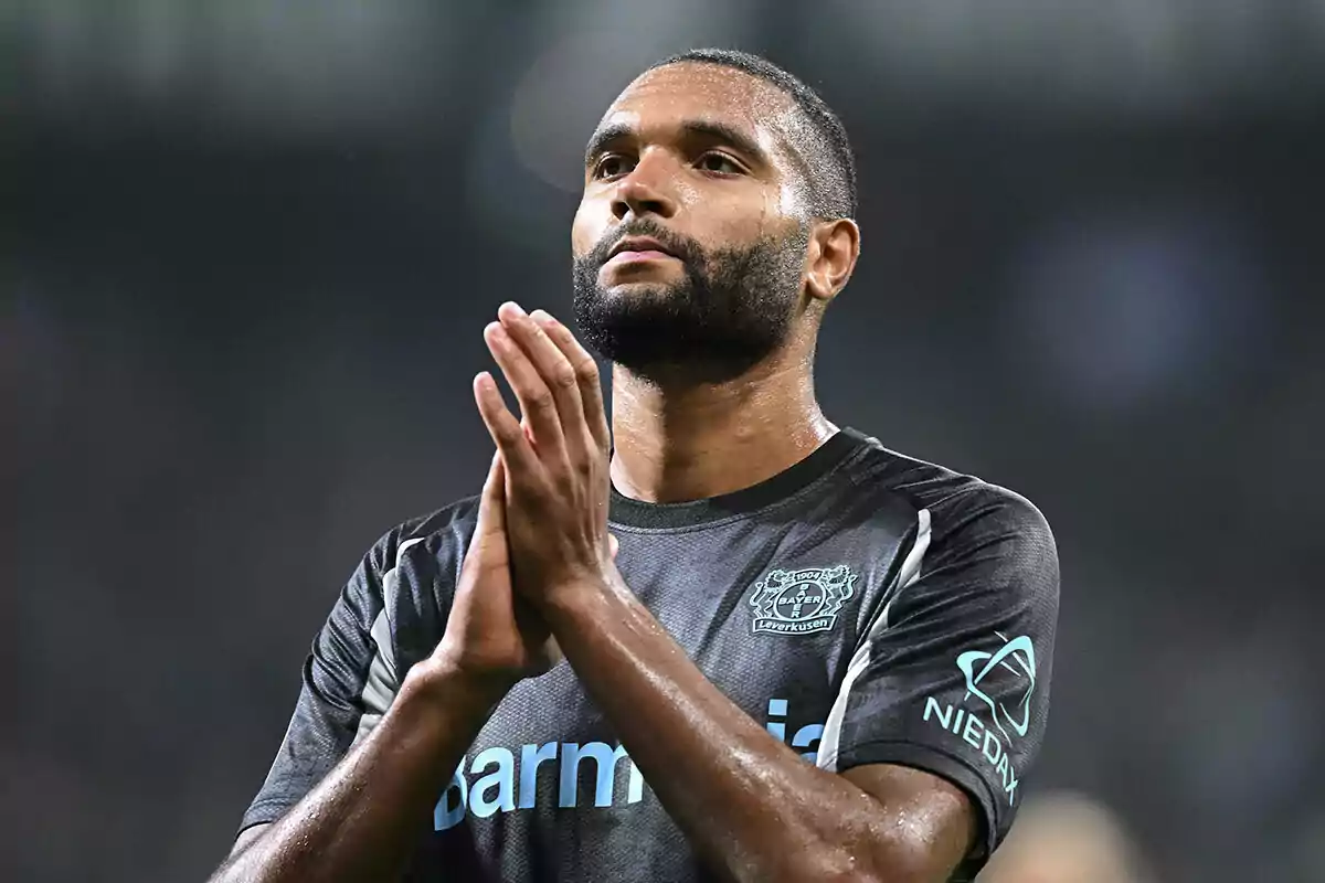 Jonathan Tah con uniforme negro aplaude en el campo.