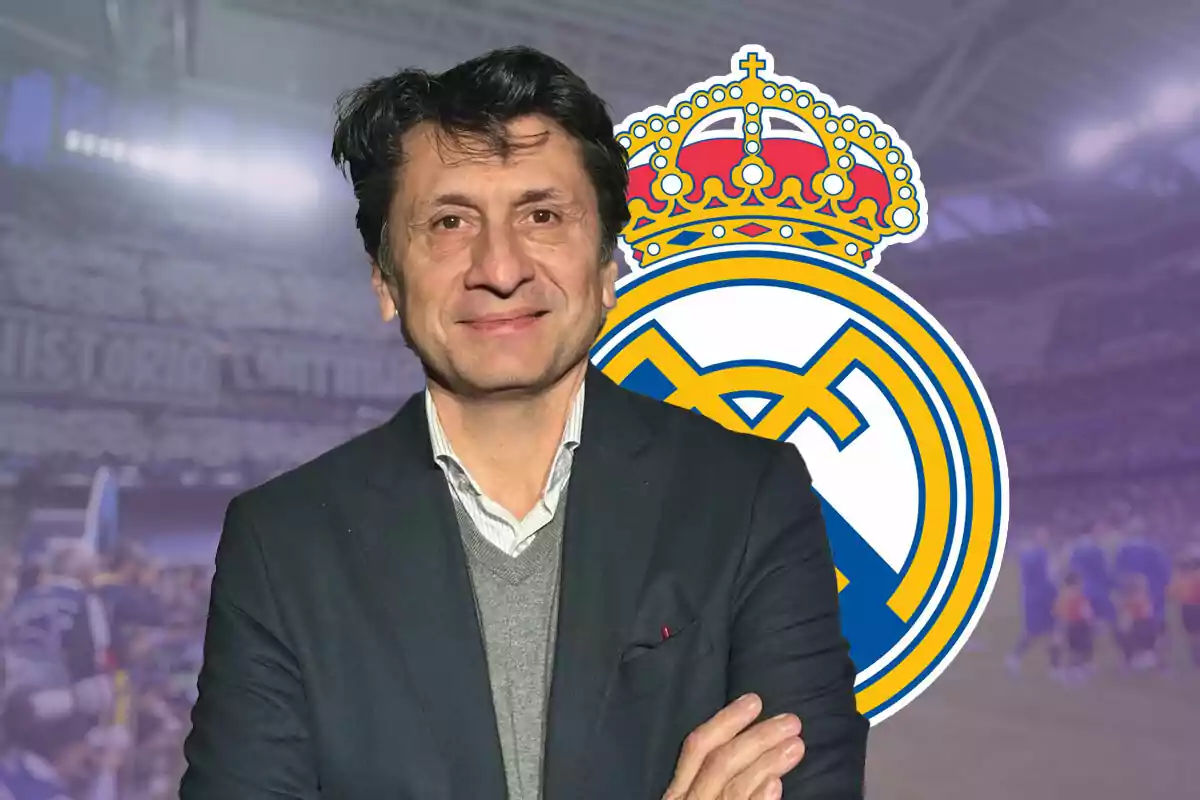 José Félix Díaz con traje oscuro y suéter gris posando frente al escudo del Real Madrid en un estadio.