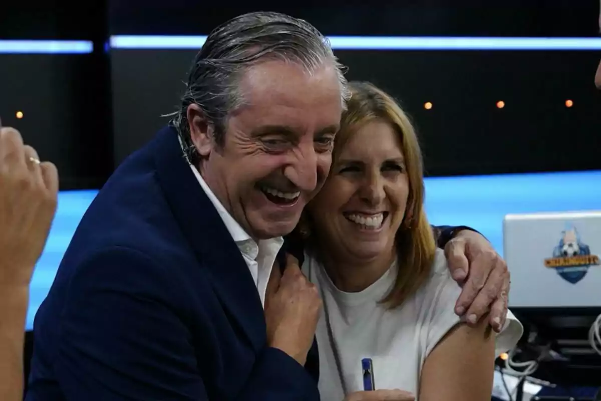 Dos personas sonríen y se abrazan en un estudio de televisión con ambiente alegre y relajado