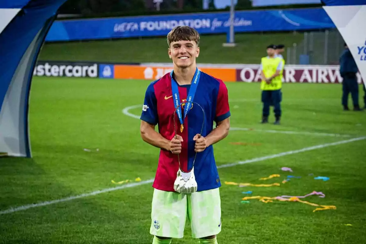 Un jugador de fútbol sonríe mientras sostiene una medalla en un campo de juego. Un jugador de fútbol sonríe mientras sostiene una medalla en un campo de juego.