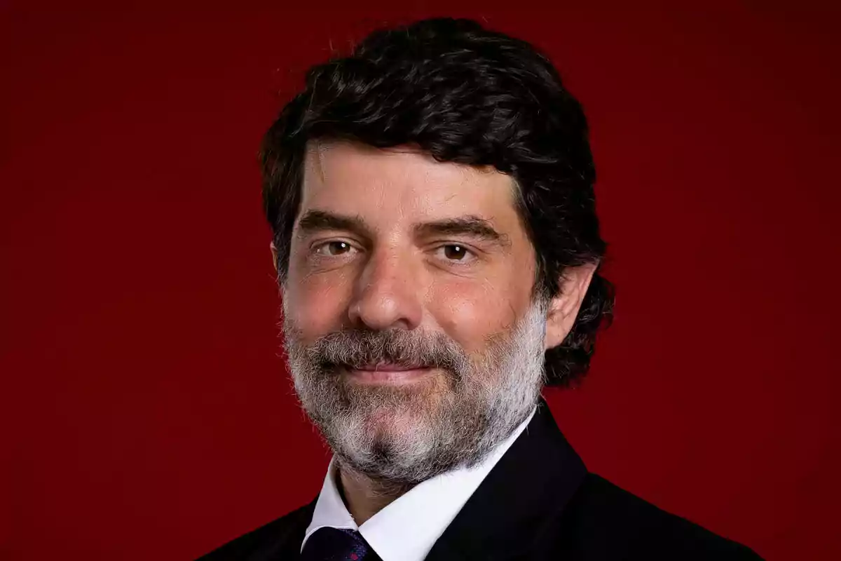 Juli Guiu with beard and dark hair dressed in a suit and tie on a red background. Juli Guiu with beard and dark hair dressed in a suit and tie on a red background.