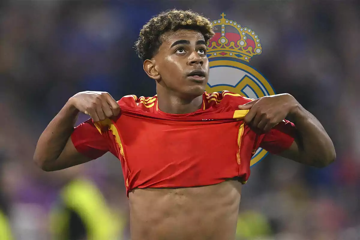 Lamine Yamal levantando su camiseta roja de España con el escudo del Real Madrid de fondo.