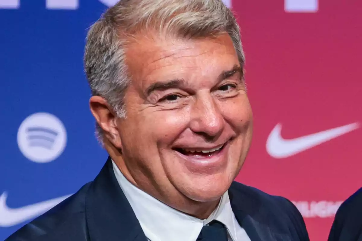 Un hombre sonriente con cabello canoso y traje oscuro frente a un fondo con logotipos.