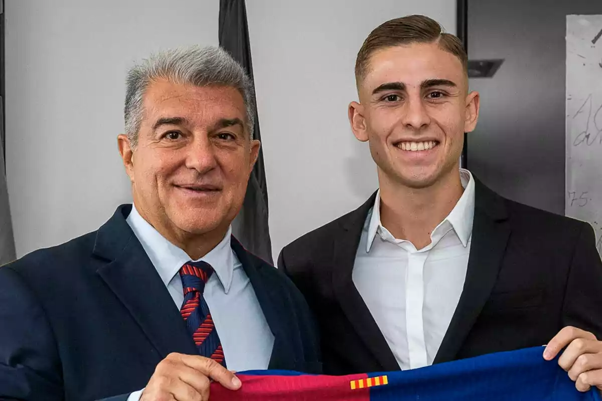 Dos hombres sonríen mientras sostienen una camiseta de fútbol.