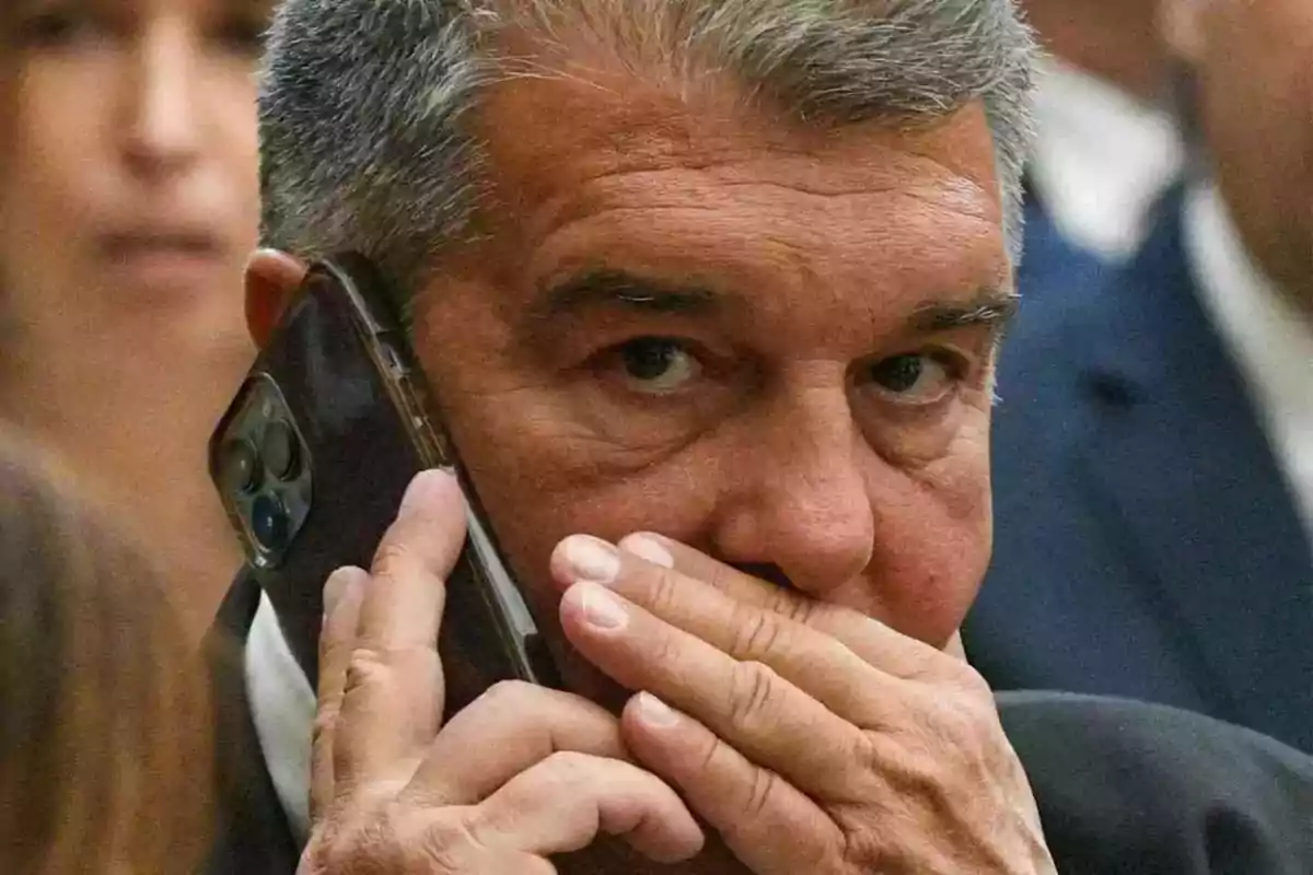 Hombre de cabello canoso hablando por teléfono y cubriéndose la boca con la mano.