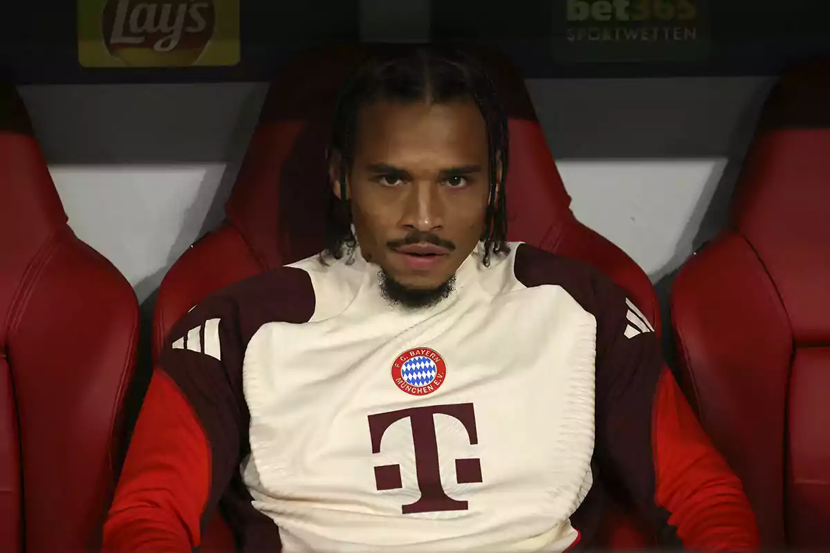 A soccer player sitting on the bench wearing a Bayern Munich sweatjersey.