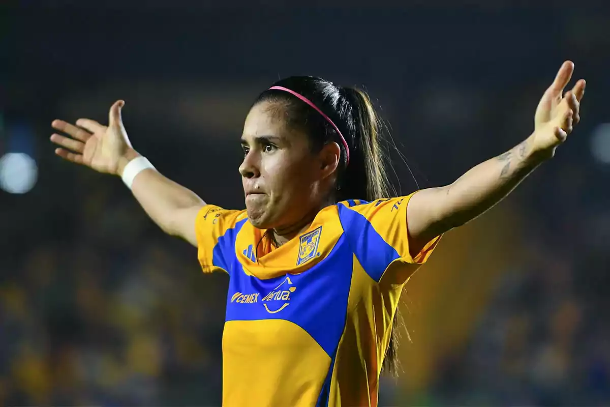 Lizbeth Ovalle in yellow and blue uniform celebrating with open arms in a stadium.