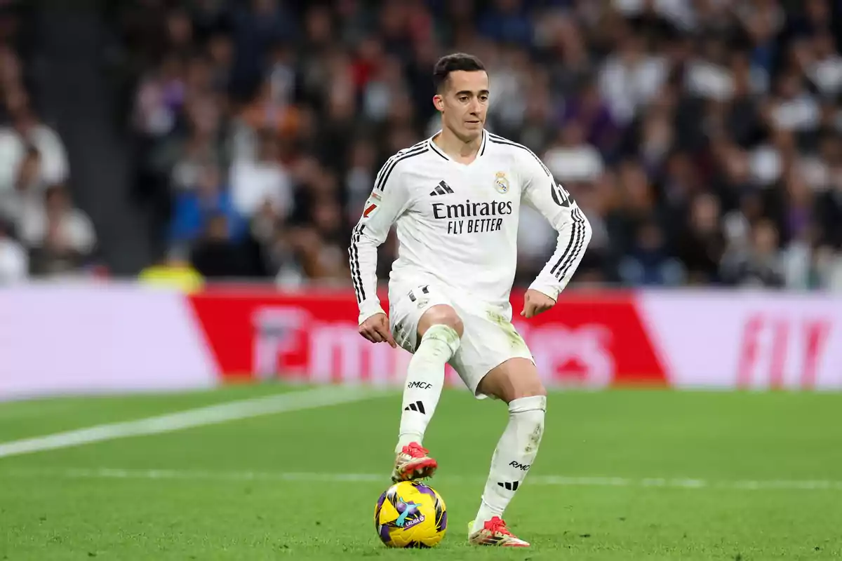 Un jugador de fútbol con uniforme blanco controla el balón en un estadio durante un partido.