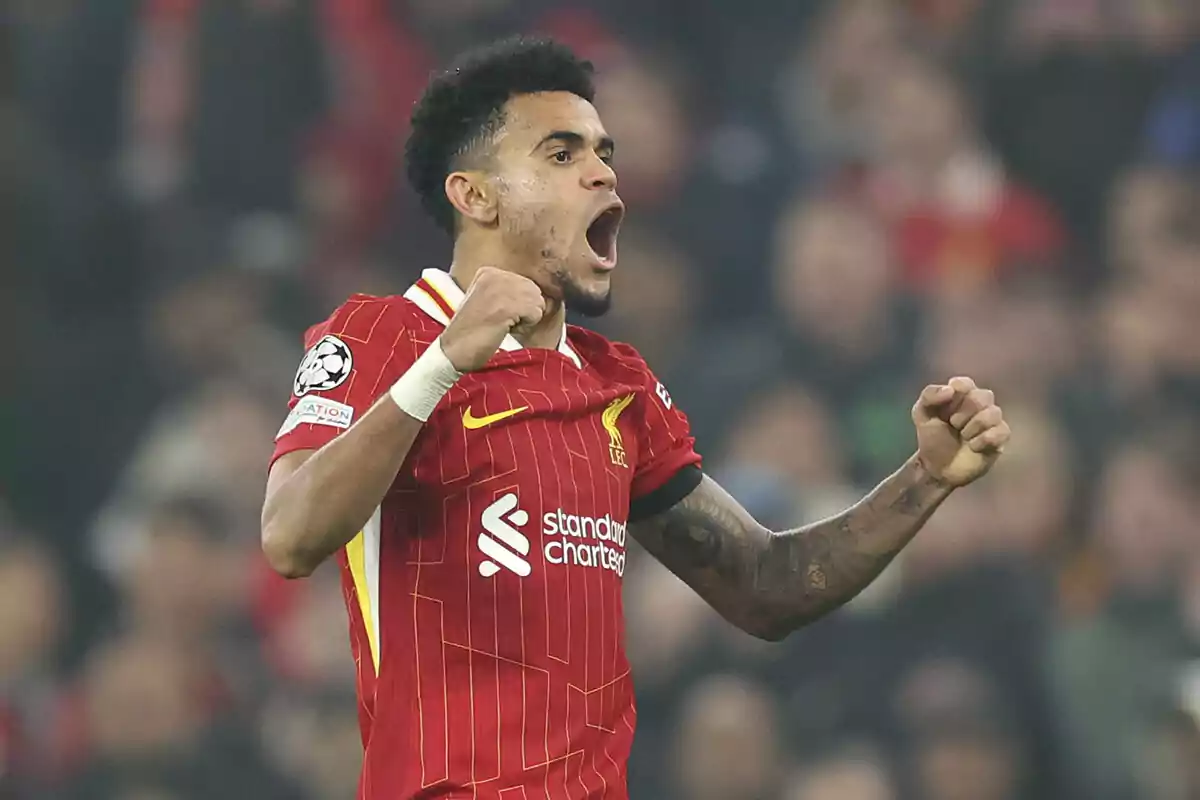 Un jugador de fútbol con uniforme rojo celebra con los puños cerrados en un estadio.