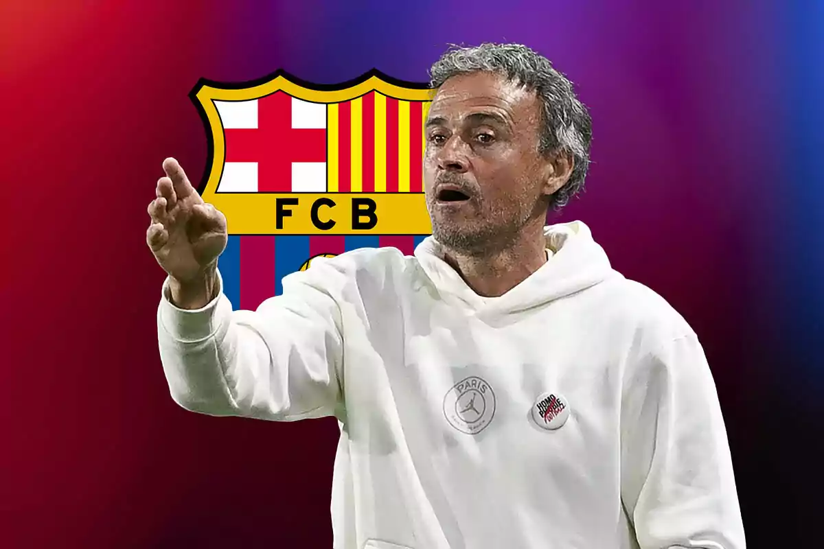 Luis Enrique con sudadera blanca gesticulando con la mano frente al escudo del FC Barcelona.