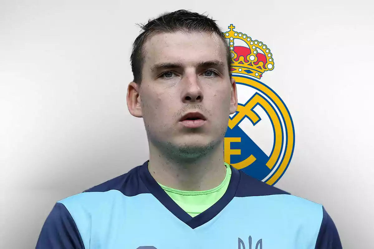 Andriy Lunin con uniforme azul claro y escudo del Real Madrid de fondo.