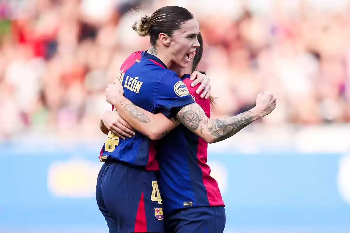 Dos jugadoras de fútbol celebran un gol abrazándose en el campo, vistiendo uniformes del FC Barcelona.