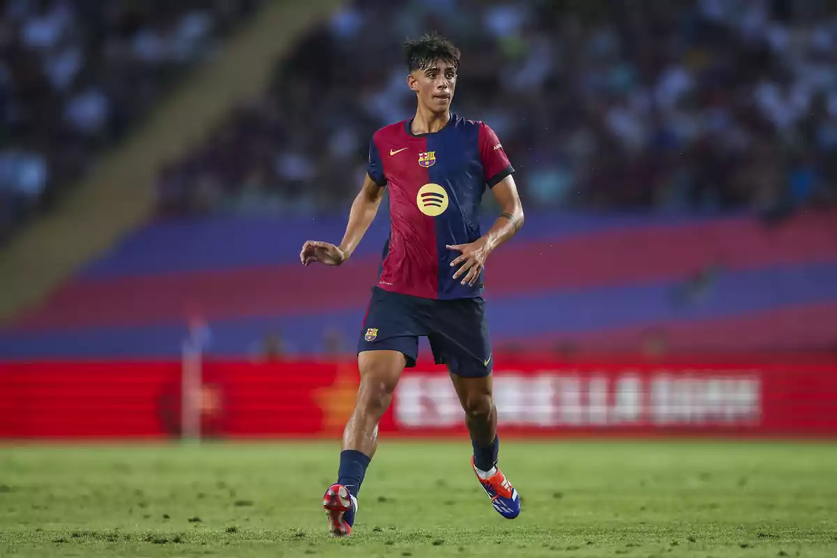 Jugador del FC Barcelona con uniforme azul y rojo corriendo en el campo durante un partido de fútbol con el estadio lleno de espectadores al fondo Jugador del FC Barcelona con uniforme azul y rojo corriendo en el campo durante un partido de fútbol con el estadio lleno de espectadores al fondo
