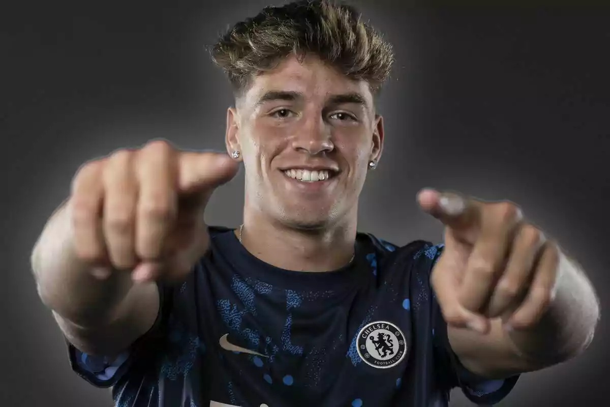 Joven con camiseta del Chelsea sonriendo y señalando hacia la cámara con ambas manos