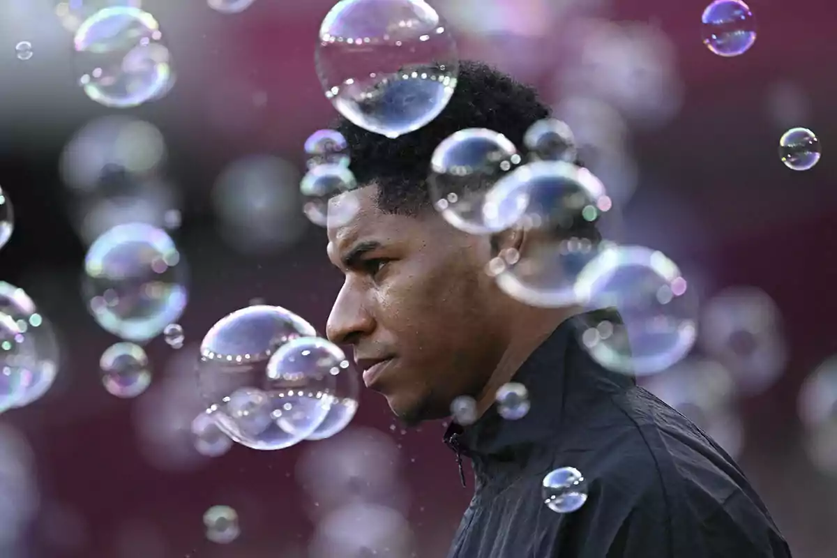 Marcus Rashford in a dark jacket surrounded by bubbles in an out-of-focus environment.