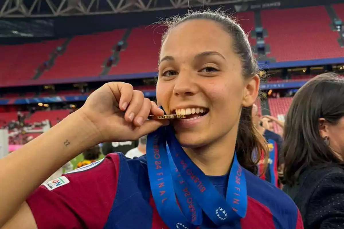 A smiling Martina Fernández bites a medal in a sports stadium. A smiling Martina Fernández bites a medal in a sports stadium.