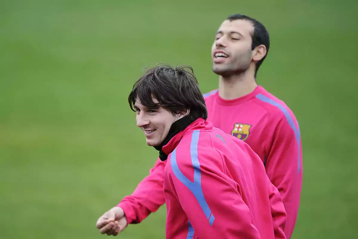 Two soccer players in pink training uniforms smile as they stand on a grass field.