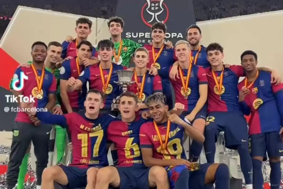 Barcelona players celebrate with medals and a trophy after winning the Spanish Super Cup, posing and smiling in front of a tournament banner. Barcelona players celebrate with medals and a trophy after winning the Spanish Super Cup, posing and smiling in front of a tournament banner.