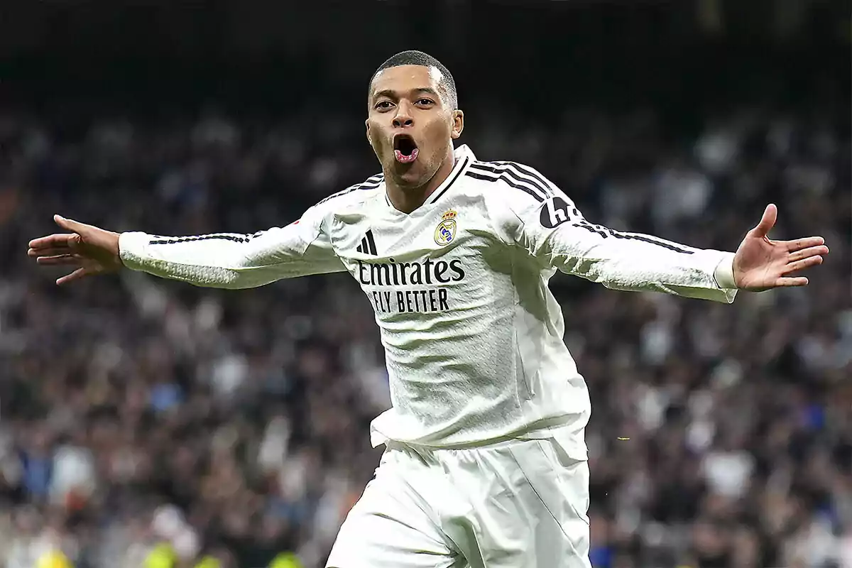 Un jugador de fútbol celebrando un gol con los brazos extendidos, vistiendo el uniforme blanco del Real Madrid.