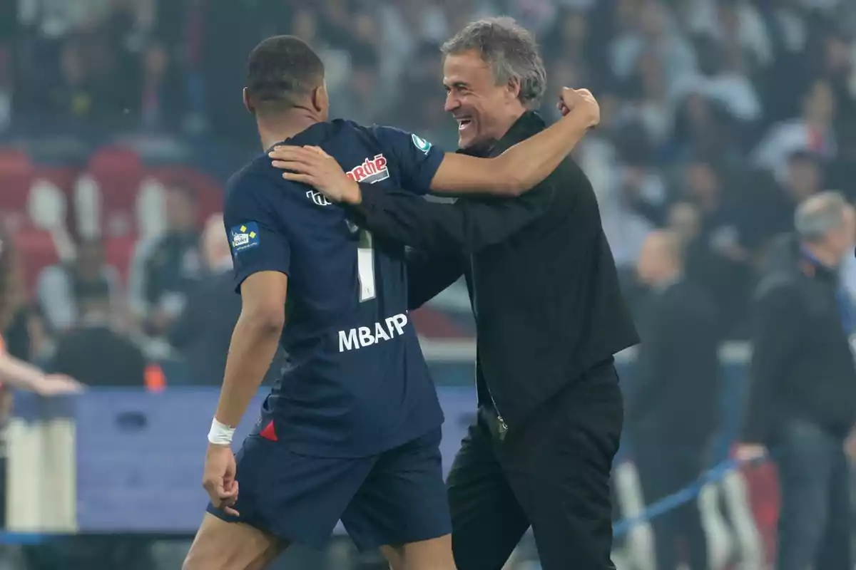 Un jugador de fútbol y un entrenador se abrazan en el campo de juego.