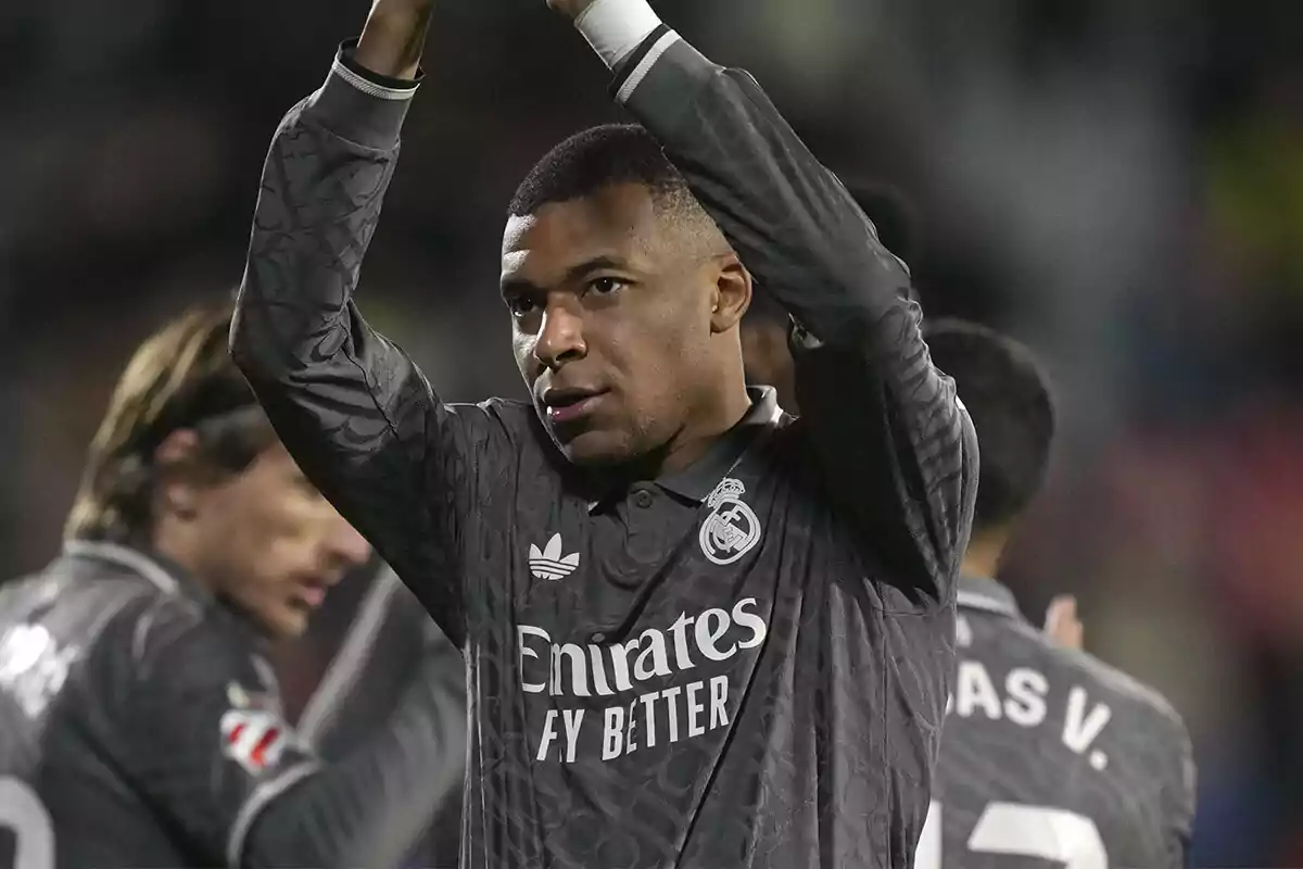 Kylian Mbappé in a grey uniform applauding on the field.