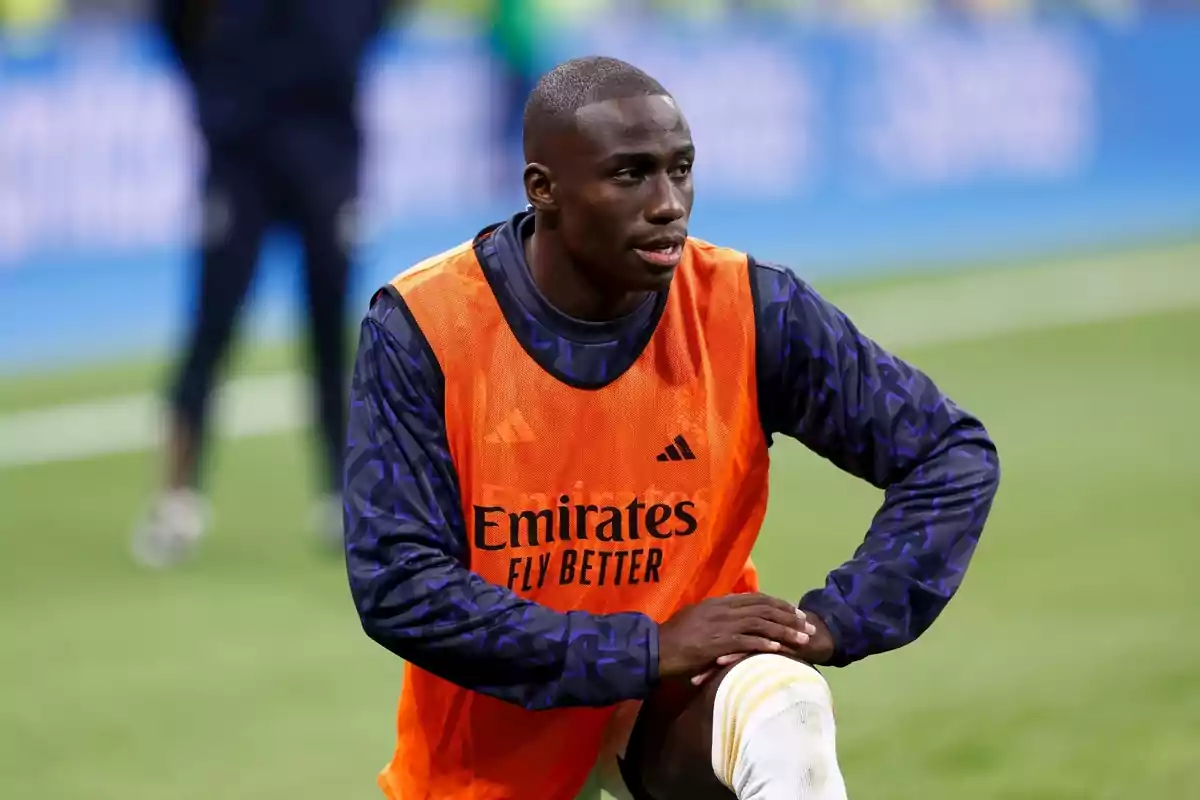 A soccer player in an orange bib prepares on the field.