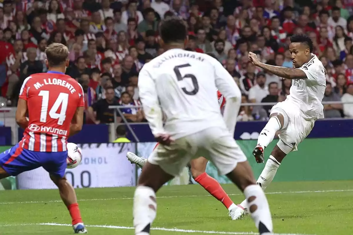 Jugadores de Atlético y Real Madrid en acción durante un partido, Militao pateando el balón mientras otros observan.