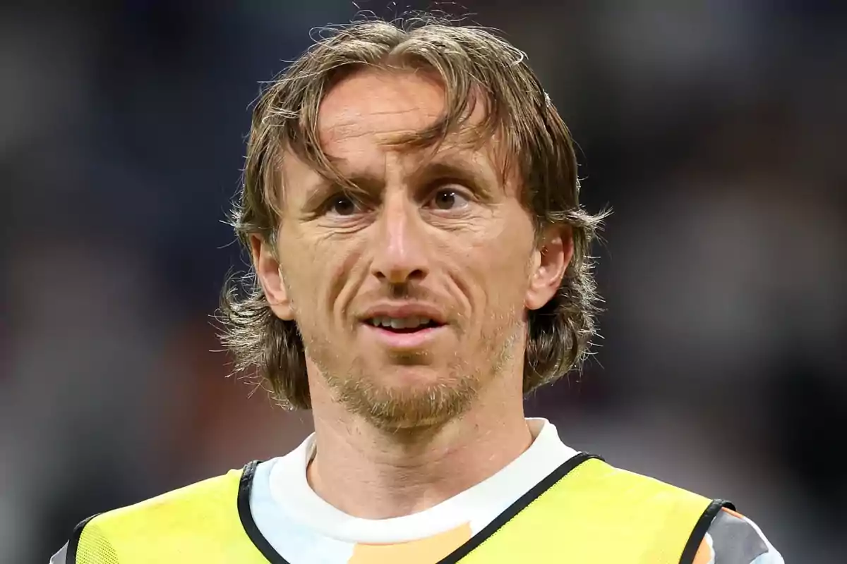 Hombre de cabello castaño y corto con chaleco deportivo amarillo en un estadio