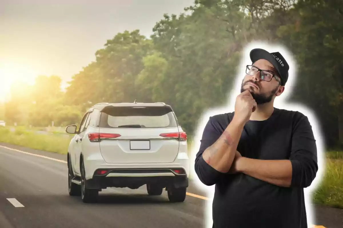 Thoughtful man in glasses and black cap, with a background of a white car on a road surrounded by trees.