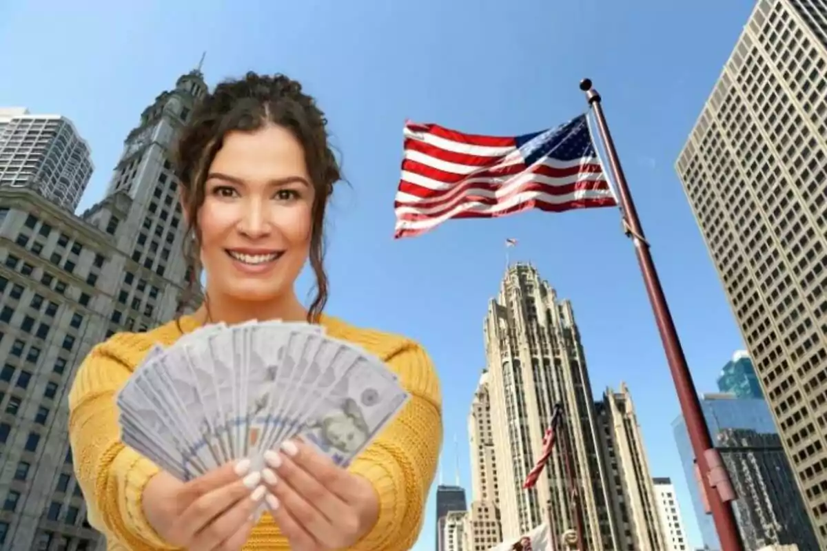 Smiling woman holds dollar bills in front of tall buildings and a United States flag on a sunny day