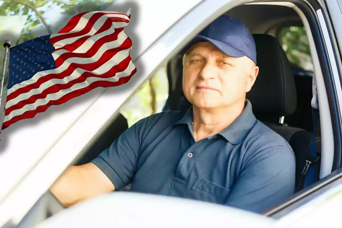 Older man with a blue cap sitting at the wheel of a car and a United States flag waving in the background