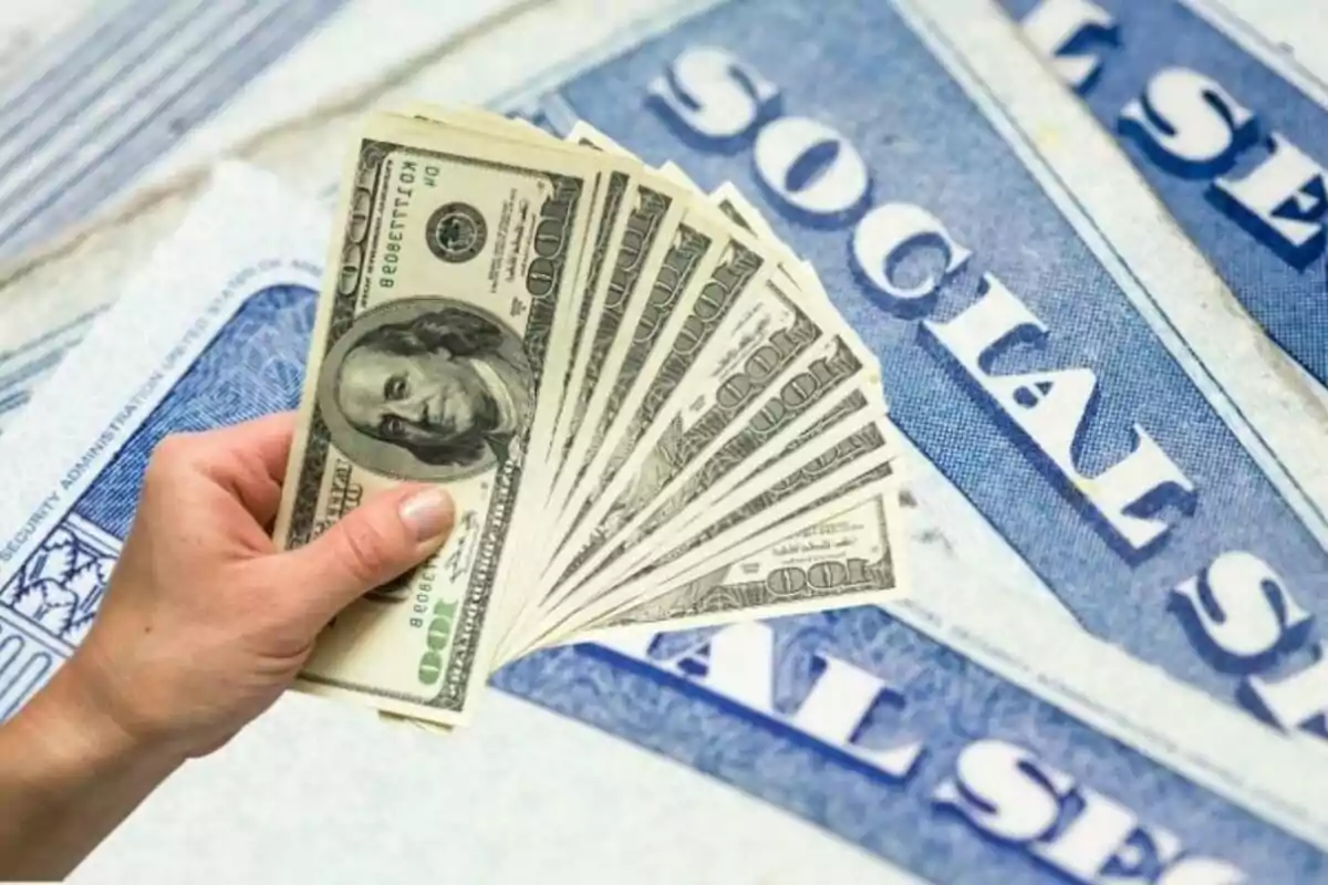 Mano sosteniendo varios billetes de cien dólares sobre tarjetas de seguro social de Estados Unidos